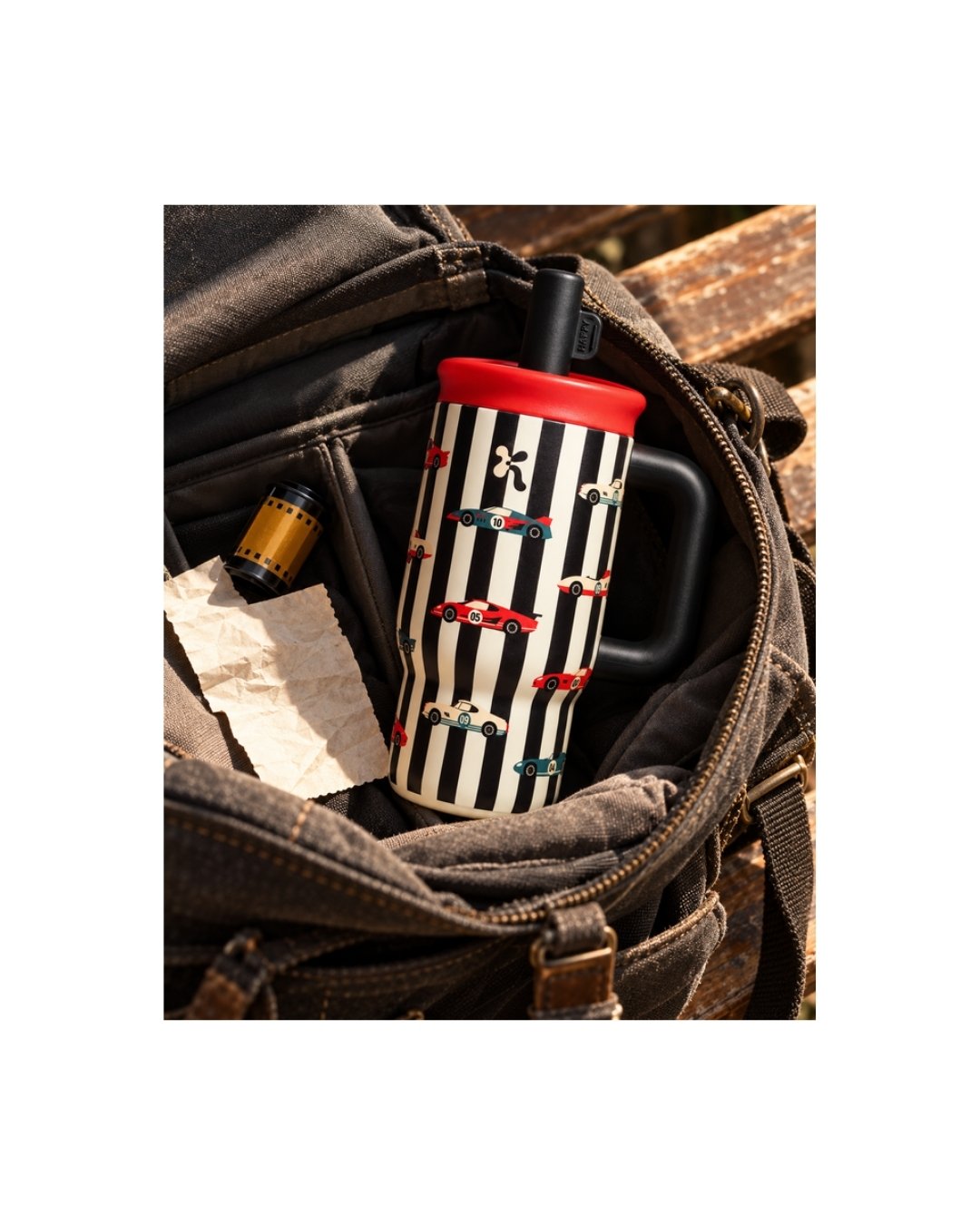 Tumbler stainless Kara Bottles motif garis hitam-putih bergambar mobil balap dengan tutup merah, terselip di dalam tas kanvas cokelat